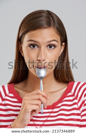 Get every last drop. Studio shot of an attractive young woman with a spoon in her mouth on a grey background.