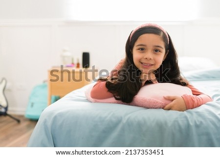 Portrait of a beautiful latin little girl smiling while relaxing in her bedroom during a leisure day   Royalty-Free Stock Photo #2137353451