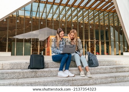 Full length view of two college classmates using a laptop sitting on the staircase of the building. Royalty-Free Stock Photo #2137354323