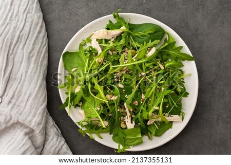 Delicious light salad with arugula and chicken breast sprinkled with various healthy seeds in a plate on a gray background, top view