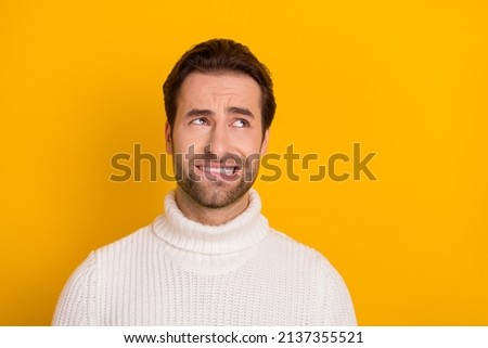 Photo of doubtful unsure guy wear white pullover biting lip looking empty space isolated yellow color background