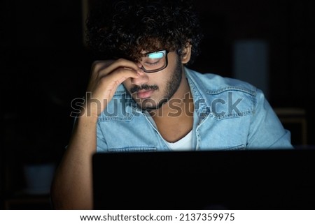 Tired sleepy stressed overworked young indian business man student wearing glasses feeling lack of sleep, having eyestrain vision problem, using laptop computer working late at night at home office. Royalty-Free Stock Photo #2137359975