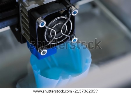 Automatic three dimensional printer machine printing blue plastic model at modern technology exhibition - close up. 3D printing, futuristic, equipment, prototype, manufacturing and production concept Royalty-Free Stock Photo #2137362059