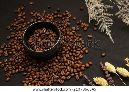 Coffee beans in a saucer and scattered around on a dark gray background. Top view