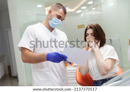 Professional doctor dentist showing a picture of teeth to a terrified woman patient