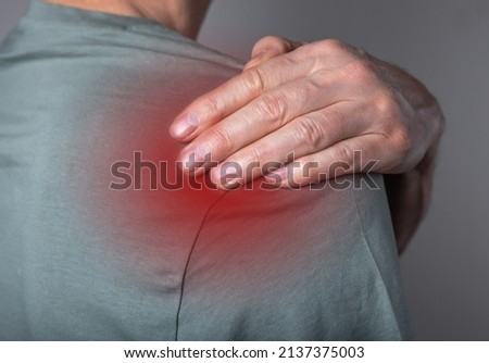 Man suffering from shoulder pain. Trigger point. Hand holding shoulder with red spot closeup. Health problems, medicine concept. High quality photo