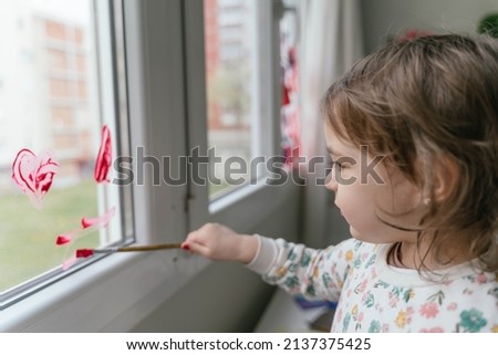 Adorable little girl painting a window