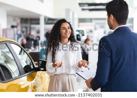 Female customer pretty arab lady with long curly hair having conversation with sales associate unrecognizable man in suit at auto dealership, young woman buying car at modern showroom, copy space Royalty-Free Stock Photo #2137402031