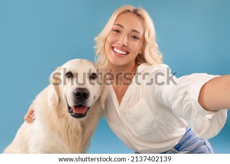 Best Friend Concept. Close up portrait of excited beautiful blonde lady hugging taking selfie with her happy labrador, posing looking at camera isolated on blue studio background, webcam point of view