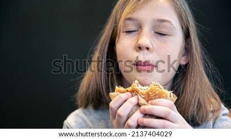 Portrait of a cute little girl with freckles, the child eats a burger, close-up.
