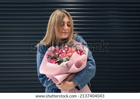 Portrait of a young woman in denim overalls with a bouquet of pink flowers on a black background, the concept of mother's day, women's day, birthday.