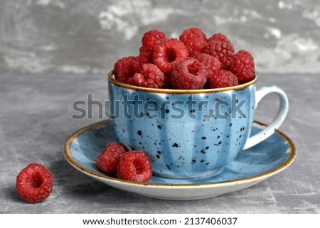 red raspberries close-up in a blue cup on a gray background