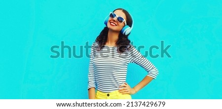 Portrait of happy smiling young woman with headphones listening to music on blue background