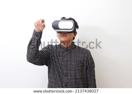 Portrait of Asian man in black plaid shirt using Virtual Reality (VR) glasses and trying to touch something in front of him. Isolated image on white background