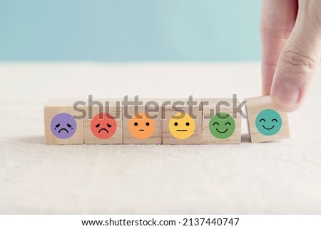 Hand choosing happy smile face wooden block, good feedback rating and positive customer review, mental health assessment, child wellness,world mental health day,think positive, emotional scale concept Royalty-Free Stock Photo #2137440747