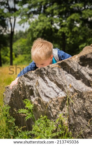 Little boy in the middle of the field on the stone forest in the background. Kid climbs on a rock, overcoming obstacles. Boy, nature, power, obstruction, stone.