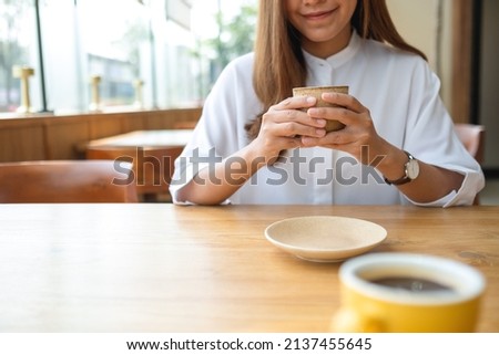 Closeup image of a young woman holding and drinking coffee in cafe