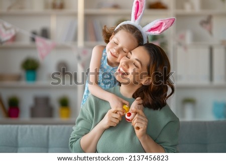 Happy holiday! Mother and her daughter with painting eggs. Family celebrating Easter. Cute little child girl is wearing bunny ears. Royalty-Free Stock Photo #2137456823
