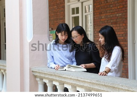 Female professor supervisor or school teacher with glasses discuss with young university girl undergraduate postgraduate students over a book at corridor of old red-brick building in campus Royalty-Free Stock Photo #2137499651