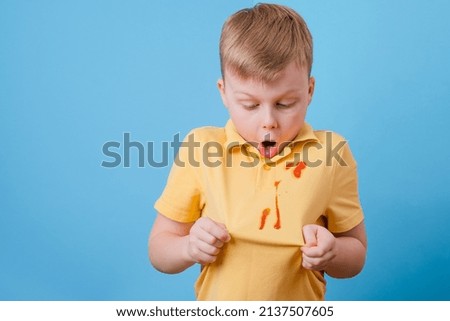 Boy showing a stain spilled from tomato sauce and spaghetti dinner on his t-shirt. The concept of cleaning stains on clothes. High quality photo Royalty-Free Stock Photo #2137507605