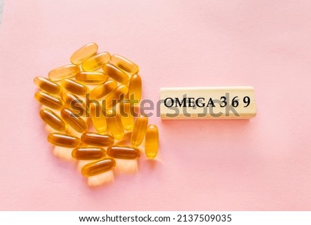Omega 3 6 9 word written on wooden cubes and golden capsules on pink background  Royalty-Free Stock Photo #2137509035