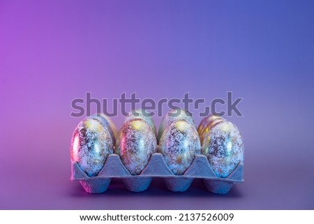 Cardboard container with Easter golden eggs with different patterns in neon colors light. Purple very peri color minimalist festive background. Modern trendy Easter. Selective focus. Copy space.