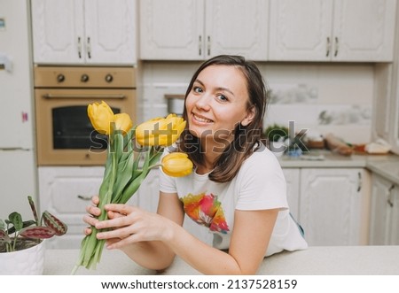 happy girl stands in the kitchen with a bouquet of yellow tulips. flowers for birthday, mother's day, easter.