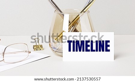 Work desk with gold glasses, pen, white card with the text TIMELINE. Business concept. Home Office. Workplace close-up.