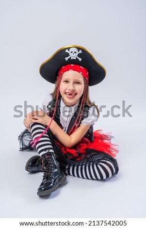 Portrait of a naughty little girl in a pirate costume, sitting on a whrite background, A girl is preparing for the Halloween holiday.