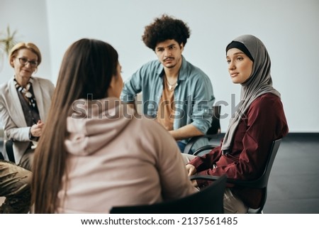 Young Muslim woman talking to group therapy members during their meeting at mental health center.  Royalty-Free Stock Photo #2137561485