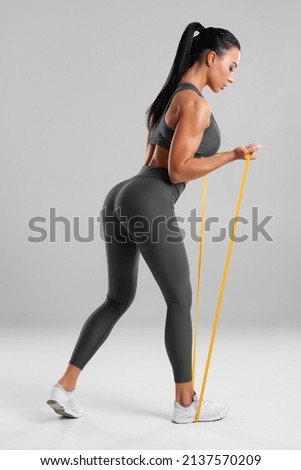 Fitness woman doing exercise with resistance band on gray background. Athletic girl working out
