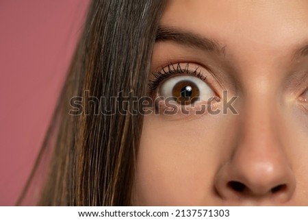 The wide open brown eye of a young woman: a concept of surprise and close observation on a pink background Royalty-Free Stock Photo #2137571303