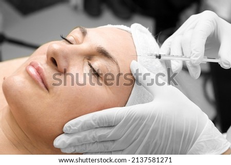 Young caucasian woman getting botox cosmetic injection in a forehead. Beautiful woman gets botox injection in her face. Adult girl gets cosmetic injection of botox in a clinic. Beauty treatments Royalty-Free Stock Photo #2137581271