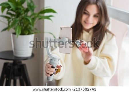 A young woman beauty blogger live broadcasted a review of cosmetics on social media. A modern female influencer shows off her daily makeup while talking to a smartphone camera. Soft selective focus.