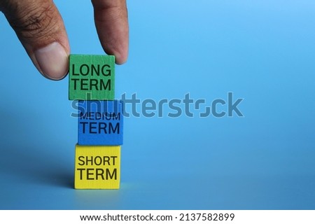 Hand pick wooden cube with text LONG TERM on blue background with copy space. Investment concept. Royalty-Free Stock Photo #2137582899