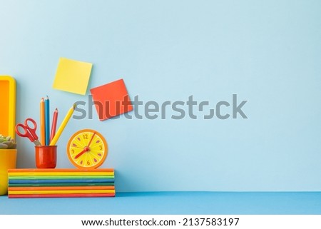 Creative desk in kids room with yellow frame mock up, plant and notebooks, note on the wall and many yellow and orange supplies. Royalty-Free Stock Photo #2137583197