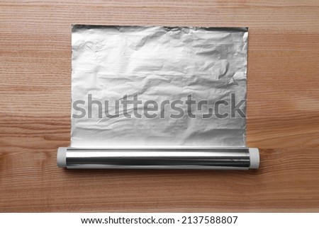 Roll of aluminum foil on wooden table, top view