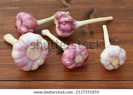 Large young garlic heads lie on a brown wooden plank table. Closeup.