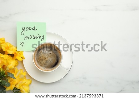 Cup of aromatic coffee, beautiful yellow freesias and Good Morning note on white marble table, flat lay. Space for text