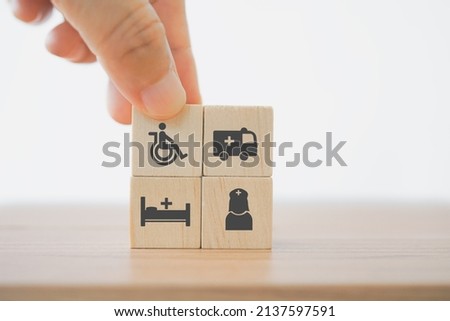 senior hand holding disability person and ambulance, bed and nurse icon on wooden cube block  for elderly care, emergency case for disabled person concept