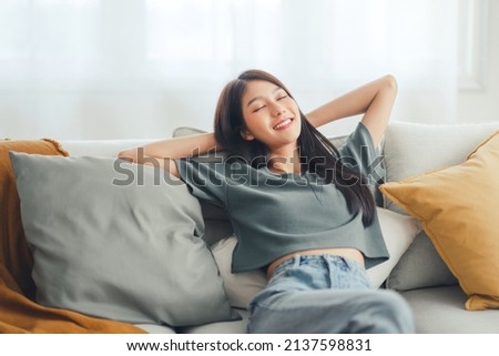 Relaxed young asian woman enjoying rest on comfortable sofa at home, calm attractive girl relaxing and breathing fresh air in home, copy space. Royalty-Free Stock Photo #2137598831