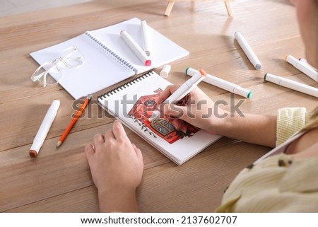 Woman drawing in sketchbook with felt tip pen at wooden table, closeup Royalty-Free Stock Photo #2137602707