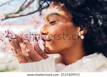 Beautiful African American woman smelling the soft, fresh and natural scent of pink flowers in spring in bloom. Concept of softness, delicacy, purity, femininity, dream of relaxation. Royalty-Free Stock Photo #2137609915