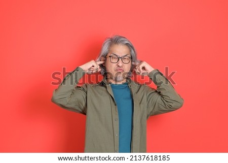 The senior Asian man with casual clothes standing on the orange background.
