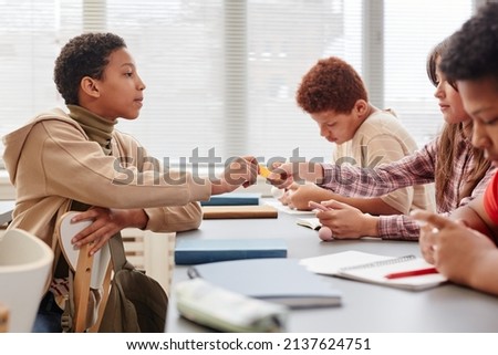 Portrait of African American teenage girl giving cheat note to friend during test in school classroom