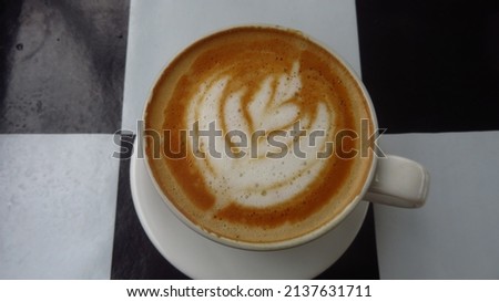 blurry and grainy picture with some color noise of square black and white pattern for a background of a white cup of coffee with a latte art caramel capucino coffe sugar