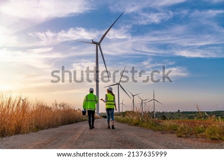 Engineer wearing uniform hold equipment box inspection work in wind turbine farms rotation to generate electricity energy. Green ecological power energy generation wind sustainable energy concept. Royalty-Free Stock Photo #2137635999