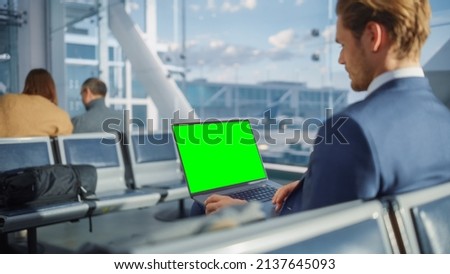 Airport Terminal: Businessman Working on Green Chroma Key Screen Laptop While Waiting for His Plane Flight. Entrepreneur Does Online Remote Work in Boarding Lounge of Airline Hub. Over the Shoulder