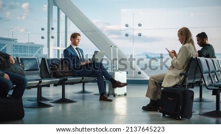 Busy Airport Terminal: Handsome Businessman Working on Laptop Computer While Waiting for His Flight. People Sitting in a Boarding Lounge of Big Airline Hub with Airplanes Departing and Arriving Royalty-Free Stock Photo #2137645223