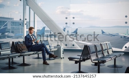 Airport Terminal Flight Wait: Smiling Businessman Uses Digital Tablet Computer for e-Business, Browsing Internet with App. Traveling Entrepreneur Work Online, Sitting in Boarding Lounge of Airline Hub Royalty-Free Stock Photo #2137645257